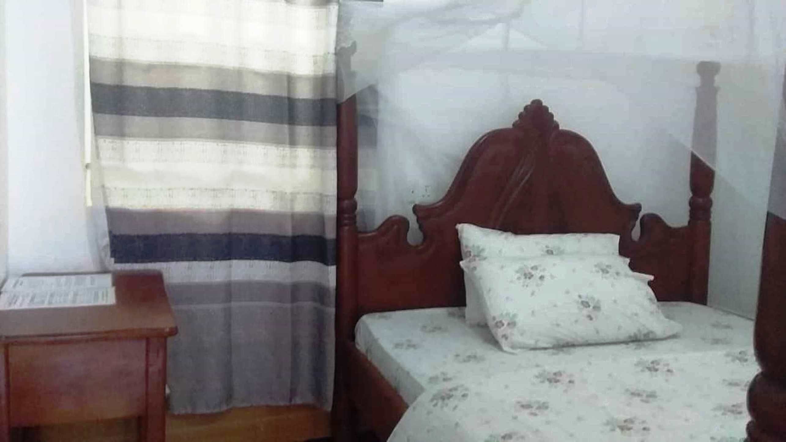 A bedroom with a wooden bed, a nightstand, and a striped curtain.