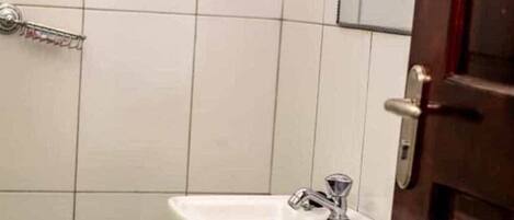 A bathroom with white tiled walls, a white sink with a chrome faucet, and a wooden door.