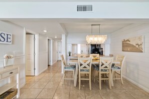 A modern kitchen with a dining area, featuring a chandelier, white cabinetry, and a tiled floor.