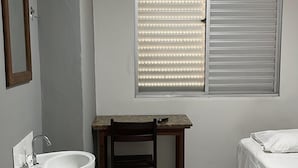 Un bany petit i net amb un lavabo blanc, una taula de fusta i un llit amb roba de llit blanca.