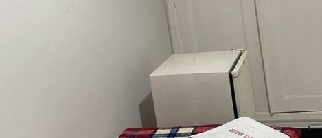 Ein kleines Zimmer mit einem Einzelbett, einem an der Wand befestigten Fernseher, einem Kleiderschrank und einem Nachttisch.