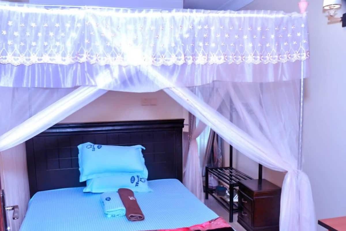 Una cama con dosel, almohadas, una toalla enrollada y una mesita de noche.