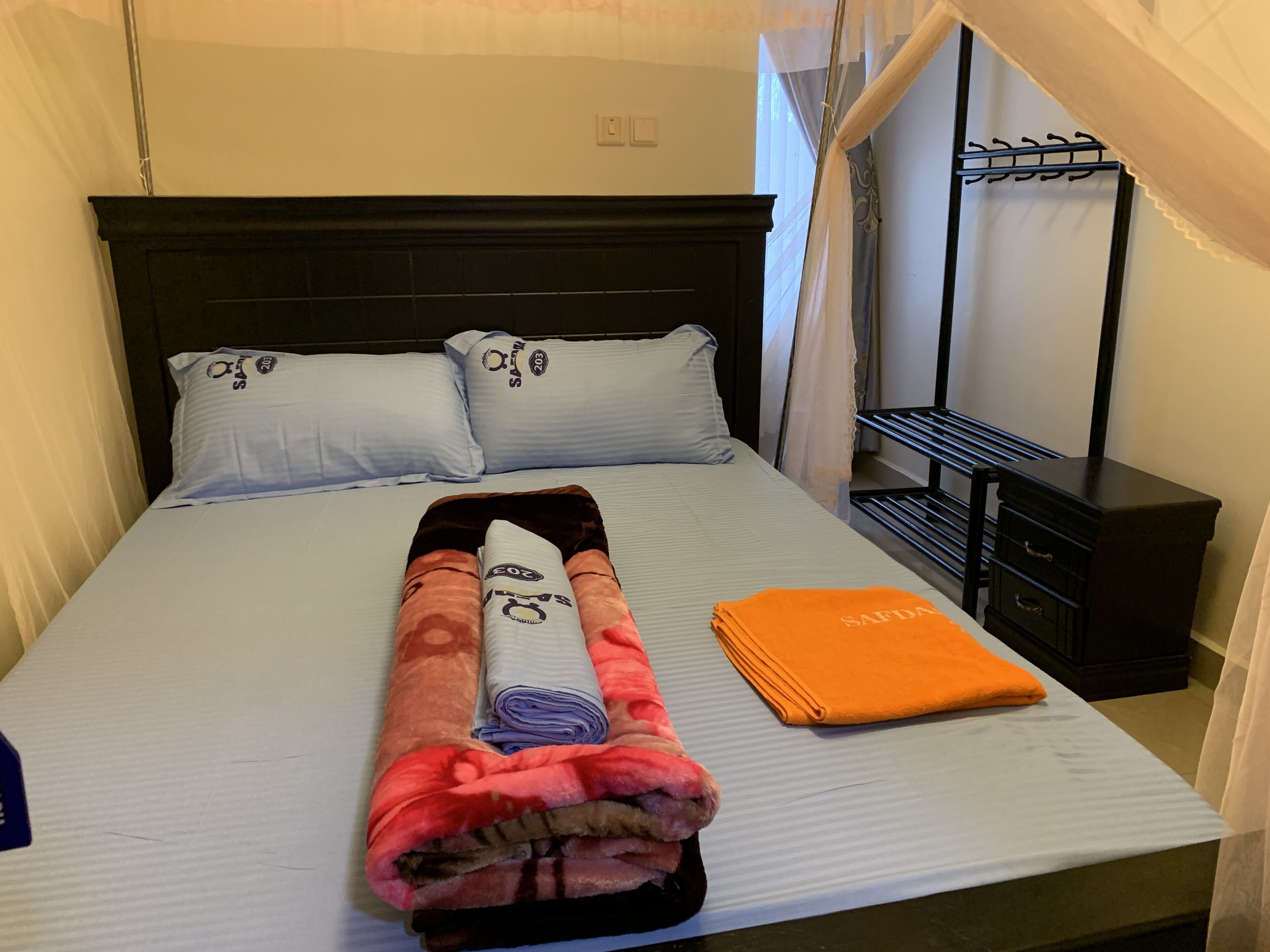 Una cama bien hecha con una colcha doblada, dos almohadas y una toalla naranja.