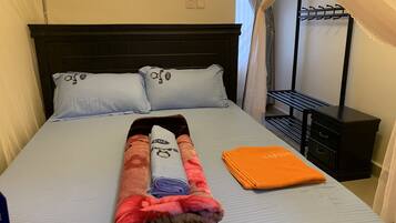 Una cama bien hecha con una colcha doblada, dos almohadas y una toalla naranja.