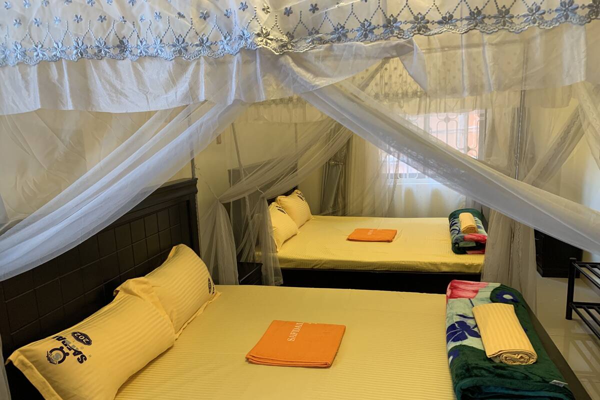 Una habitación con dos camas, cada una con dosel y una colcha amarilla. Hay una toalla naranja doblada sobre la cama en primer plano.