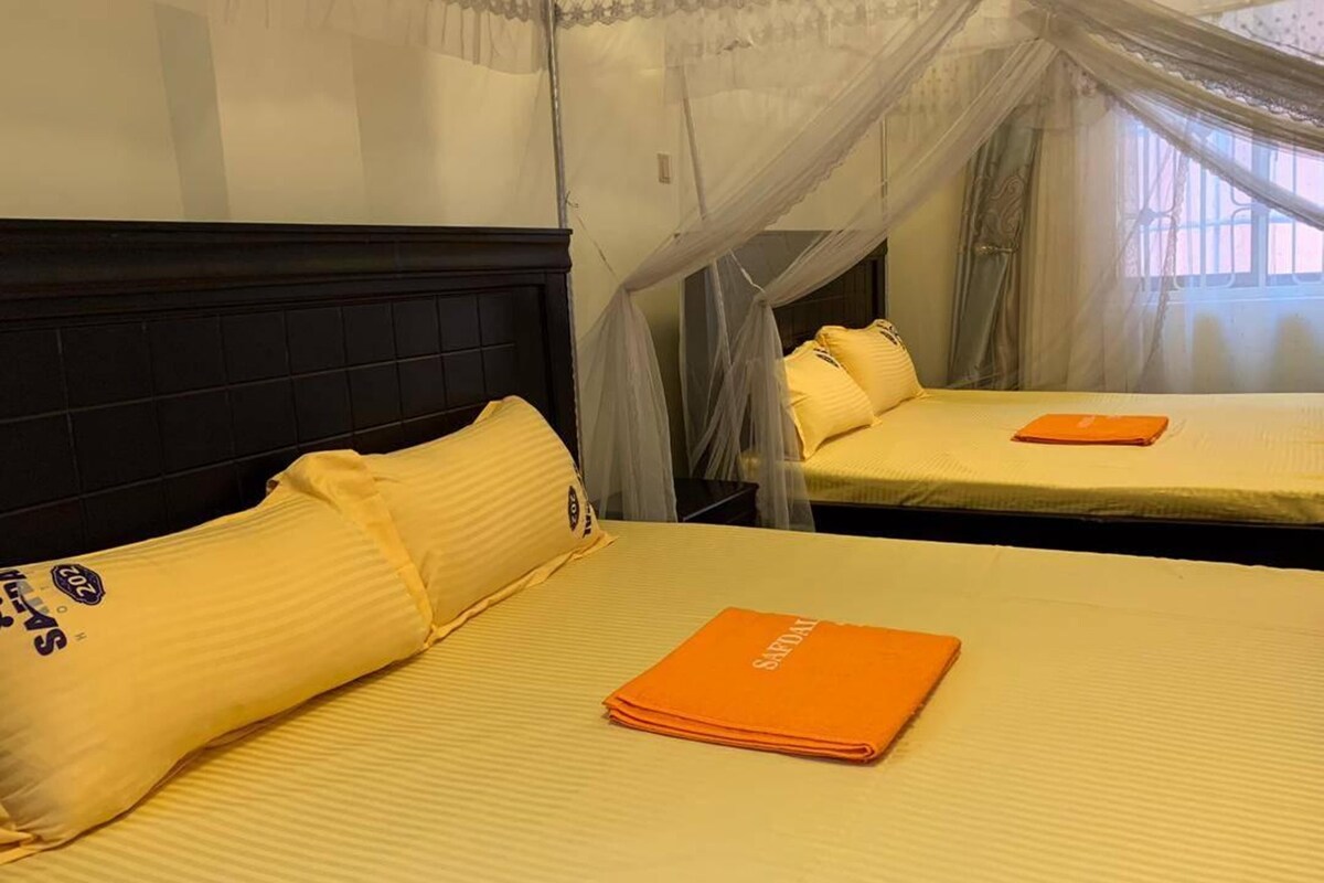 Een hotelkamer met twee bedden, elk met geel beddengoed en een hemelbed.