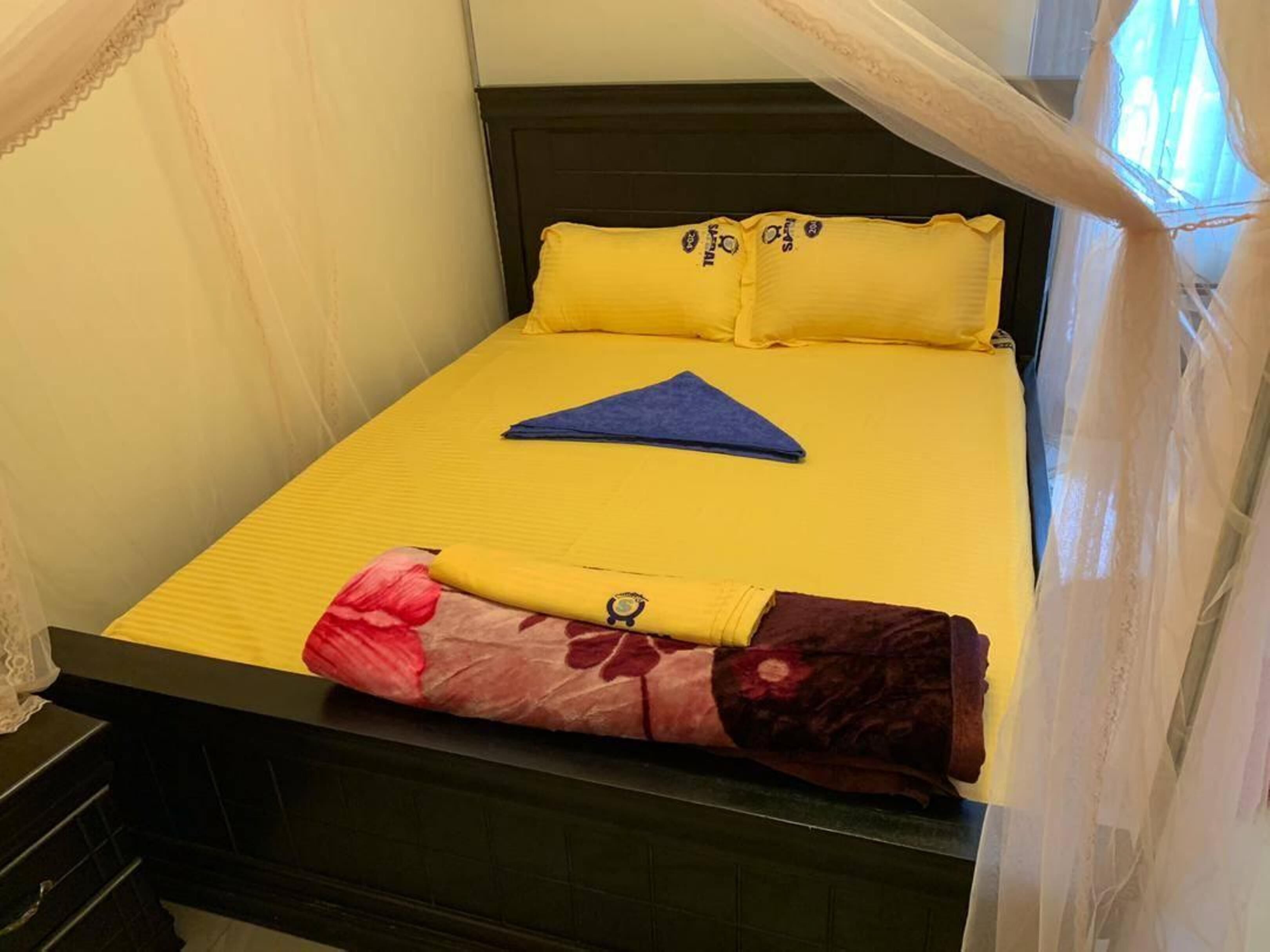A bed with yellow bedding, a blue towel, and floral-patterned pants folded at the foot.