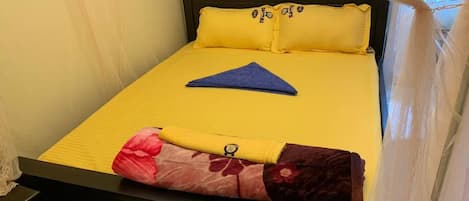 A bed with yellow bedding, a blue towel, and floral-patterned pants folded at the foot.