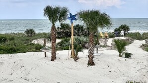 Une plage bordée de palmiers, une girouette bleue décorative et deux chaises de plage.