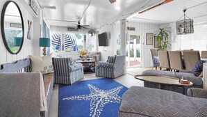Un vaste espace de vie agrémenté de fauteuils à rayures, d’un tapis orné de motifs d’étoiles de mer et d’un ventilateur de plafond.