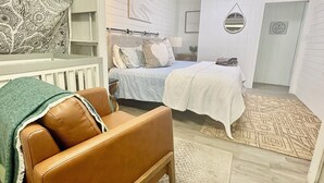 Une chambre à coucher comprenant un lit, une table de chevet, une commode, un miroir et un mur orné d’une tapisserie décorative.