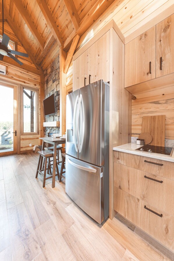A modern kitchen with wooden cabinets, a stainless steel refrigerator, and a stone wall.