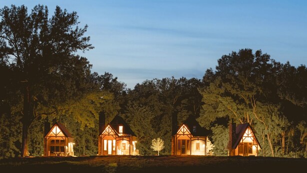 A row of three illuminated cabins by a calm lake at dusk.