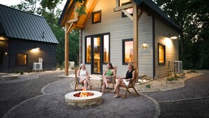 A cozy outdoor seating area with a fire pit, surrounded by a stone patio, in front of a wooden cabin-style building with large windows and a stone facade.