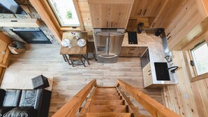 A compact kitchen with wooden cabinets, a stainless steel refrigerator, and a dining area with a table and chairs. - #10 Hummingbird Hideaway (Dahinda)