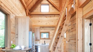 A wooden cabin interior with a dining area, kitchen, and a staircase leading to an upper level. - #10 Hummingbird Hideaway (Dahinda)