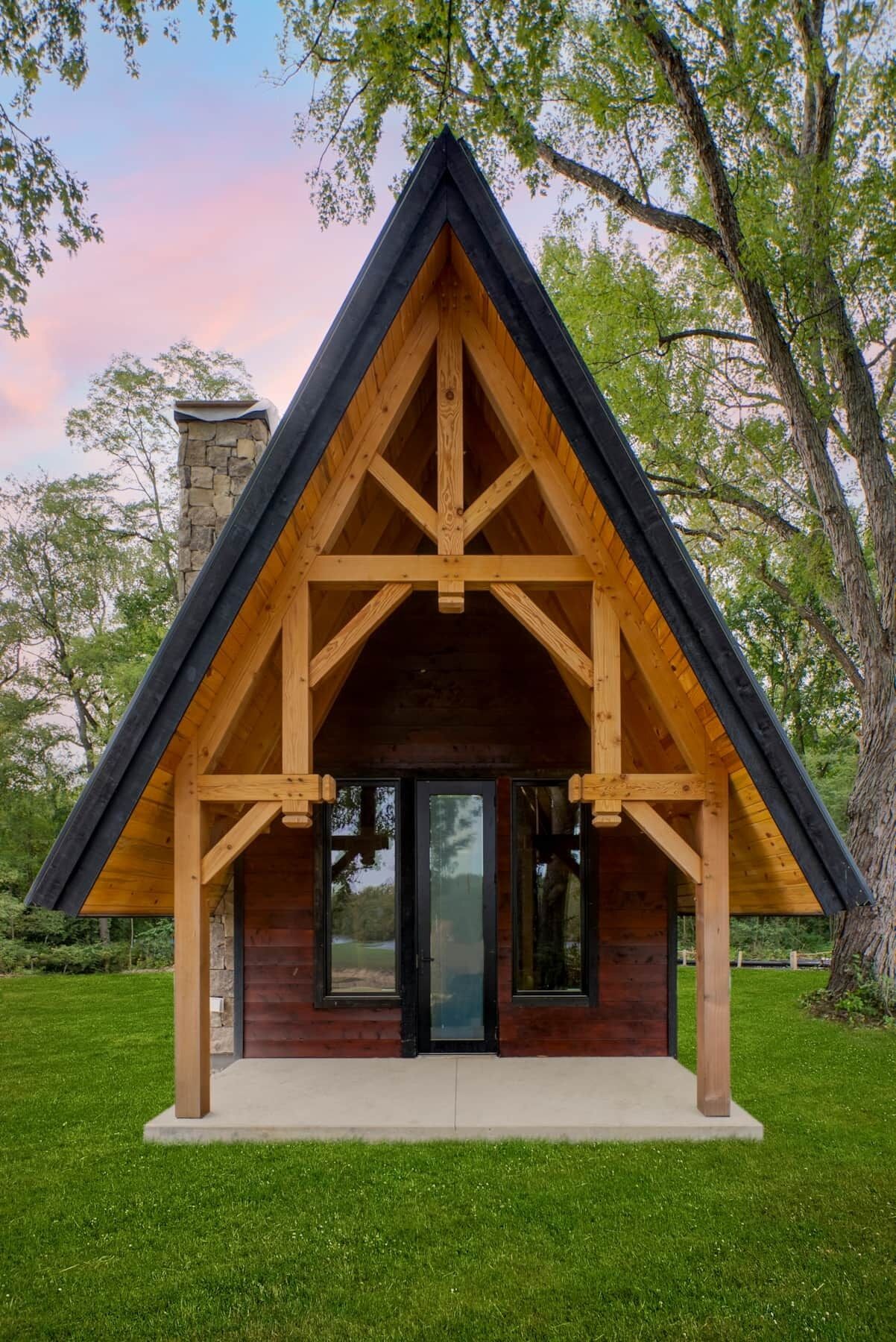 A wooden cabin with a pitched roof, large windows, and a stone chimney.