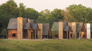 A row of rustic cabins with stone walls and metal roofs, set in a grassy area with trees in the background.