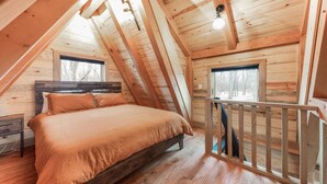 A cozy attic bedroom with a wooden bed, a nightstand, and a window overlooking a snowy landscape.