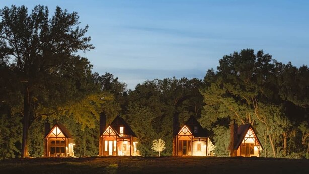 A row of three lit cottages by a calm lake at dusk.
