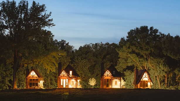 A row of three lit cottages by a calm lake at dusk.