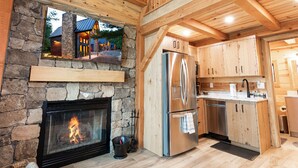 A cozy cabin interior with a stone fireplace, wooden beams, and a modern kitchen.