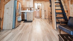 A spacious wooden cabin with a high ceiling, a central kitchen area, and a staircase leading to an upper level.