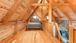 A wooden interior with a loft bedroom, stone fireplace, and wooden beams. - #16 Fox Camp (Dahinda)