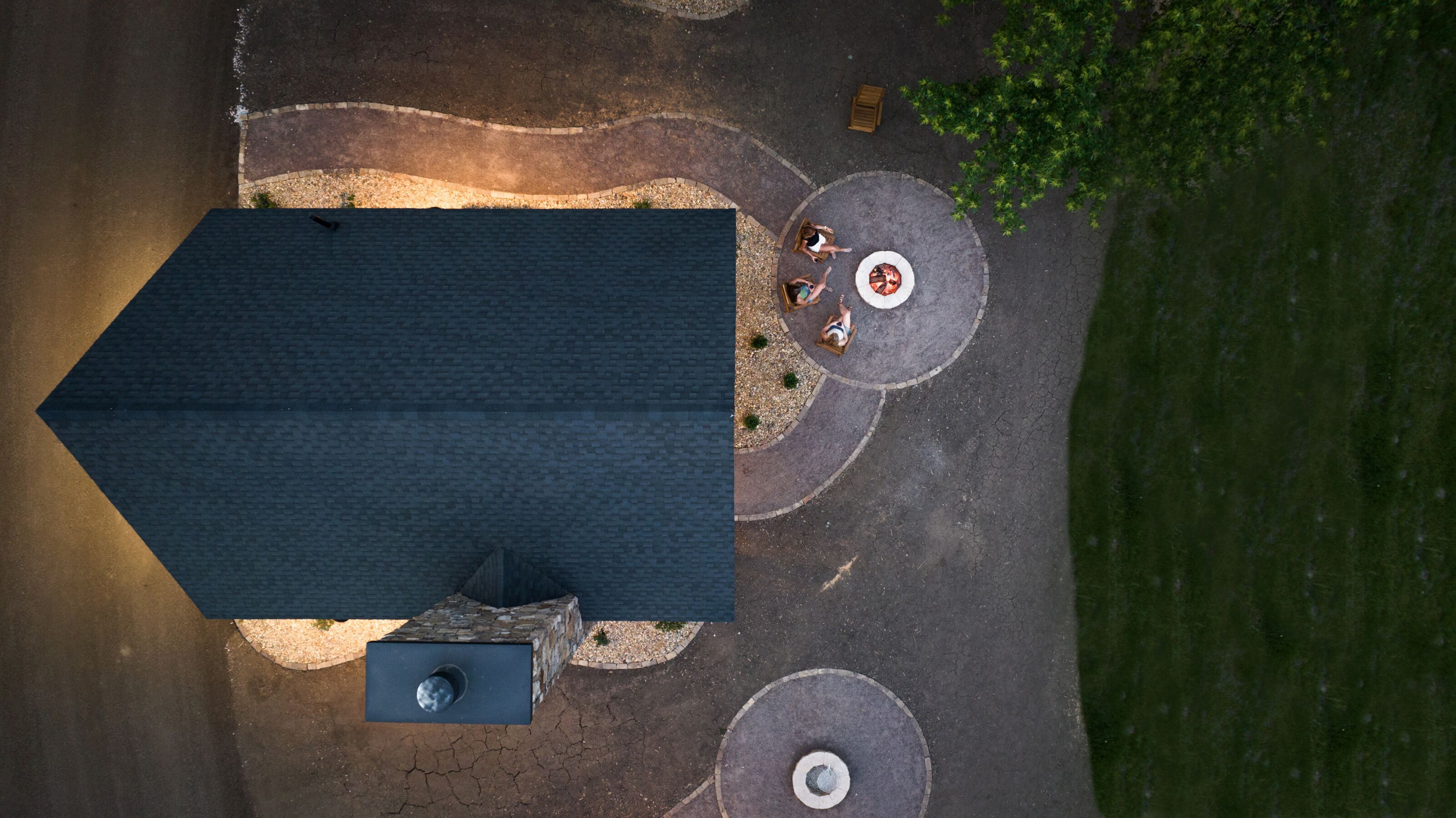 An aerial view of a building with a dark roof, a circular seating area with a table and chairs, and a small circular structure.