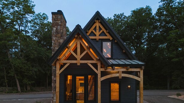 Eine kleine, dunkel gefärbte Holzhütte mit einem Steinofen, Holzbalken und einer Veranda mit einer Tür und zwei Fenstern.
