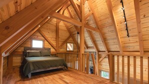 A wooden loft bedroom with a bed, wooden beams, and a window. - #20 Bluegill Cove (Dahinda)