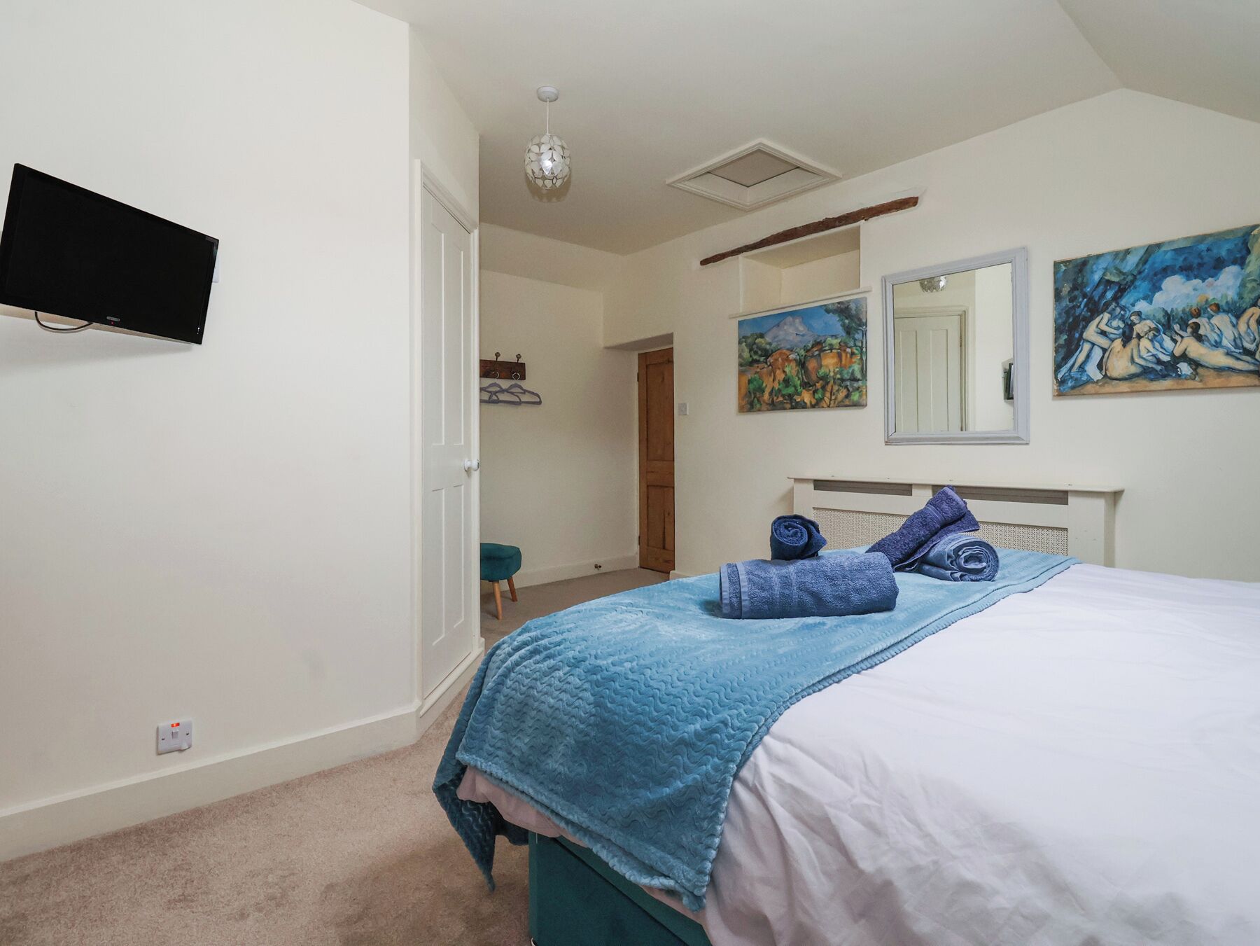 Ein Schlafzimmer mit einem Bett, einem an der Wand befestigten Fernseher und zwei Bildern.