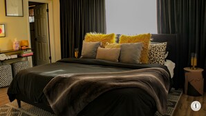 Un dormitorio con una cama grande, cortinas oscuras y una mesita de noche con lámpara.