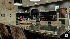 Una cocina moderna con encimera de granito, taburetes de bar y un refrigerador con una pizarra.