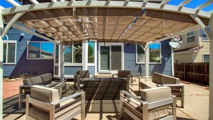 An outdoor patio with a pergola, multiple seating areas, and a view of a house with a satellite dish. - Bright&Open, Lrg home @DIA w/Pool Table & Firepit (Denver)