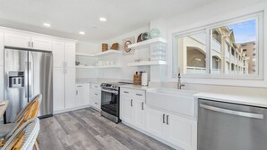 A modern kitchen with white cabinets, stainless steel appliances, and a large window offering a view of the building's architecture.