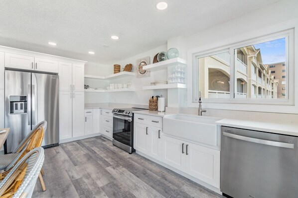 A modern kitchen with white cabinets, stainless steel appliances, and a large window offering a view of the building's architecture.