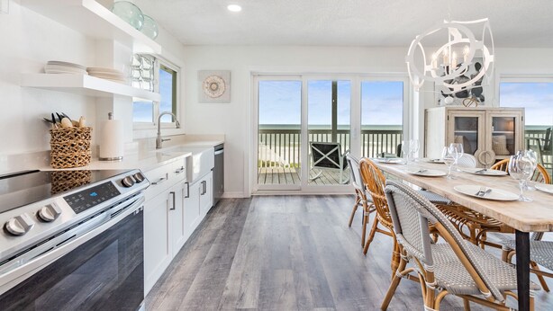 A modern kitchen with white cabinetry, a built-in oven, and a dining area with wicker chairs and a wooden table.