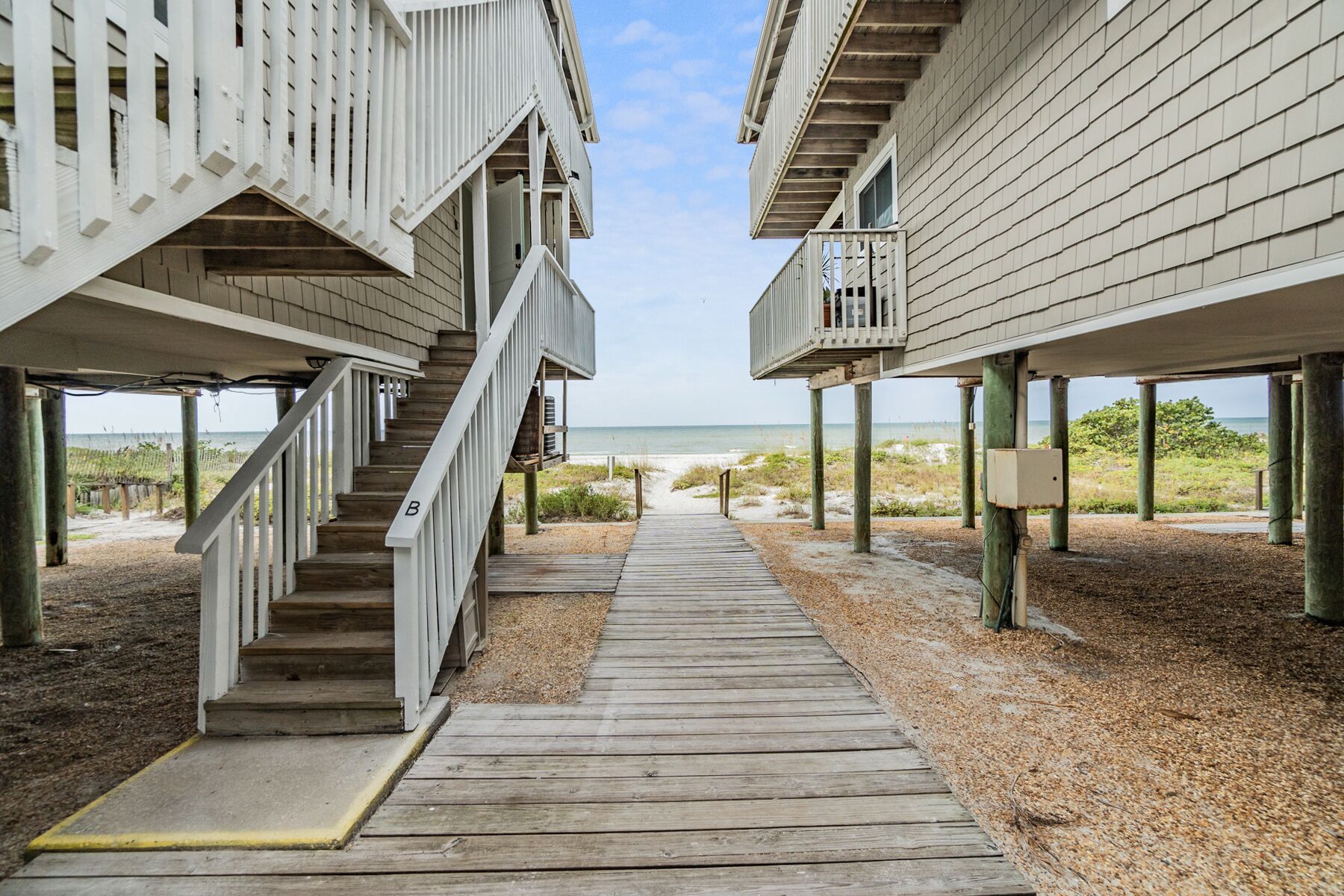 Une promenade en bois menant à des maisons de plage dotées de balcons, soutenues par des piliers.