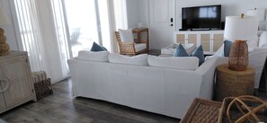 A living room with a white sofa, wicker chairs, a television, and a lamp.