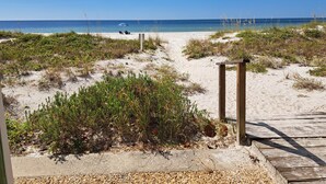 A beach pathway leading to the ocean with a wooden boardwalk and a bench.
