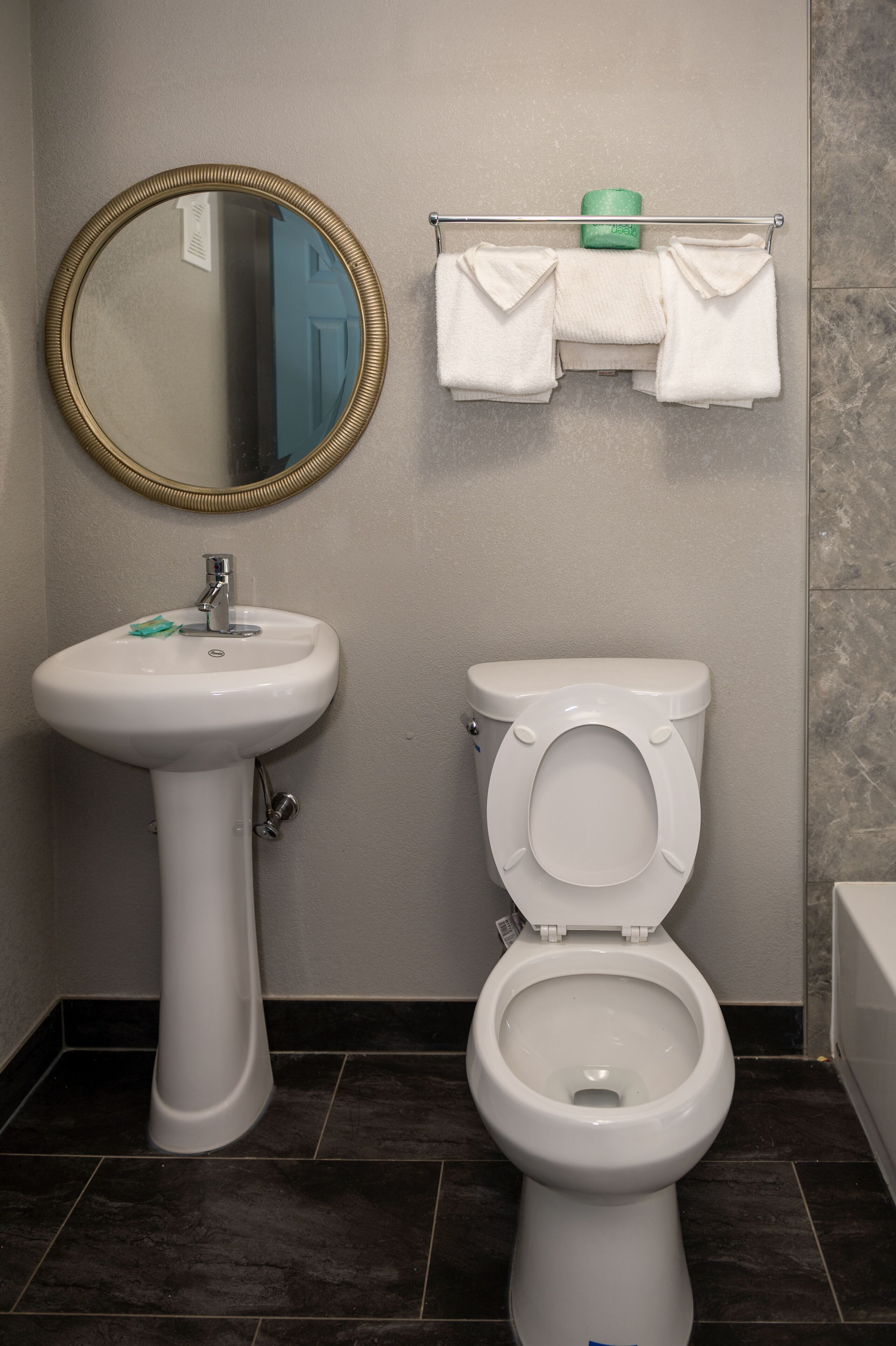 A bathroom with a pedestal sink, a toilet, a mirror, and a towel rack with towels.