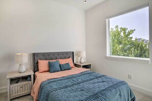 Un dormitorio con cama, mesitas de noche, una ventana y vistas a árboles.
