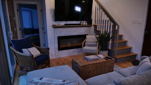 Ein Wohnzimmer mit Kamin, Fernseher, einer Couch und einer Treppe.