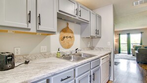 A kitchen with white cabinets, a marble countertop, and a wooden wall hanging with the word "yum."