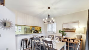 A dining area with a table set for four, surrounded by wooden chairs. A chandelier hangs from the ceiling, and a window with blinds is visible. - Sugar Mountain Chalet w/ Hot Tub & Ski Shuttle! (Sugar Mountain)