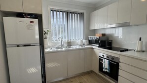 Una cocina moderna con armarios blancos, horno empotrado, un fregadero y una ventana con persianas.
