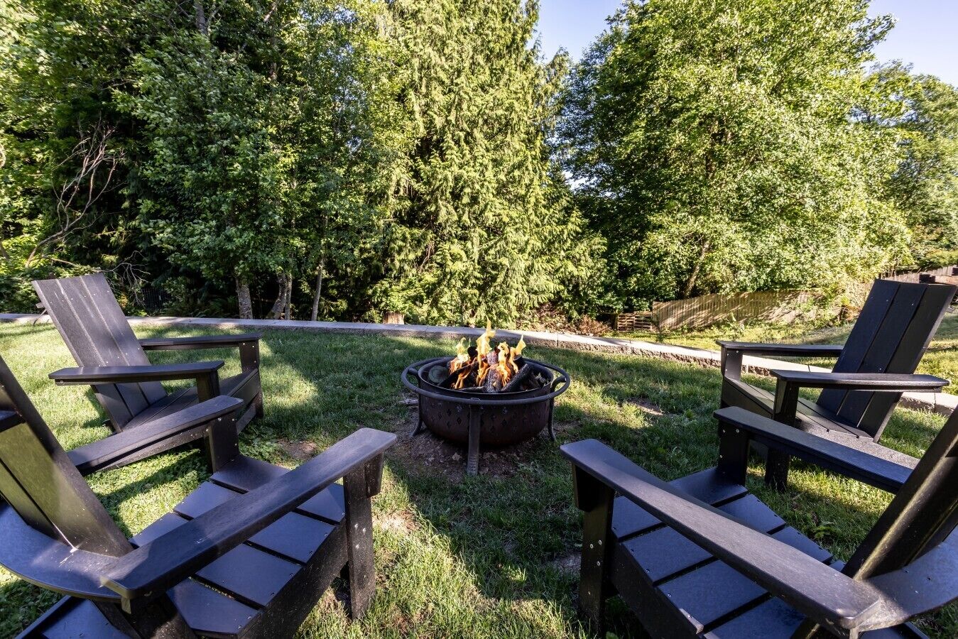 A backyard with a fire pit surrounded by Adirondack chairs.