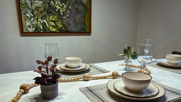 A dining table set with plates, bowls, and glasses, with a plant and a beaded string on the table. - Luxury 4BR in the Foothills · Lake & Trails · Sleeps 8 (Sedro-Woolley)