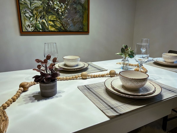 Une table à manger dressée avec des assiettes, des bols et des verres, agrémentée d’une plante et d’une guirlande de perles.